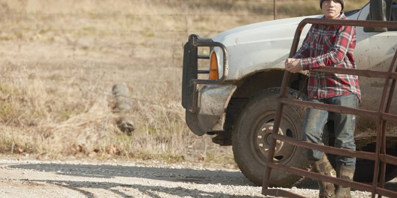 Boy farmer opening gate for truck on dairy farm